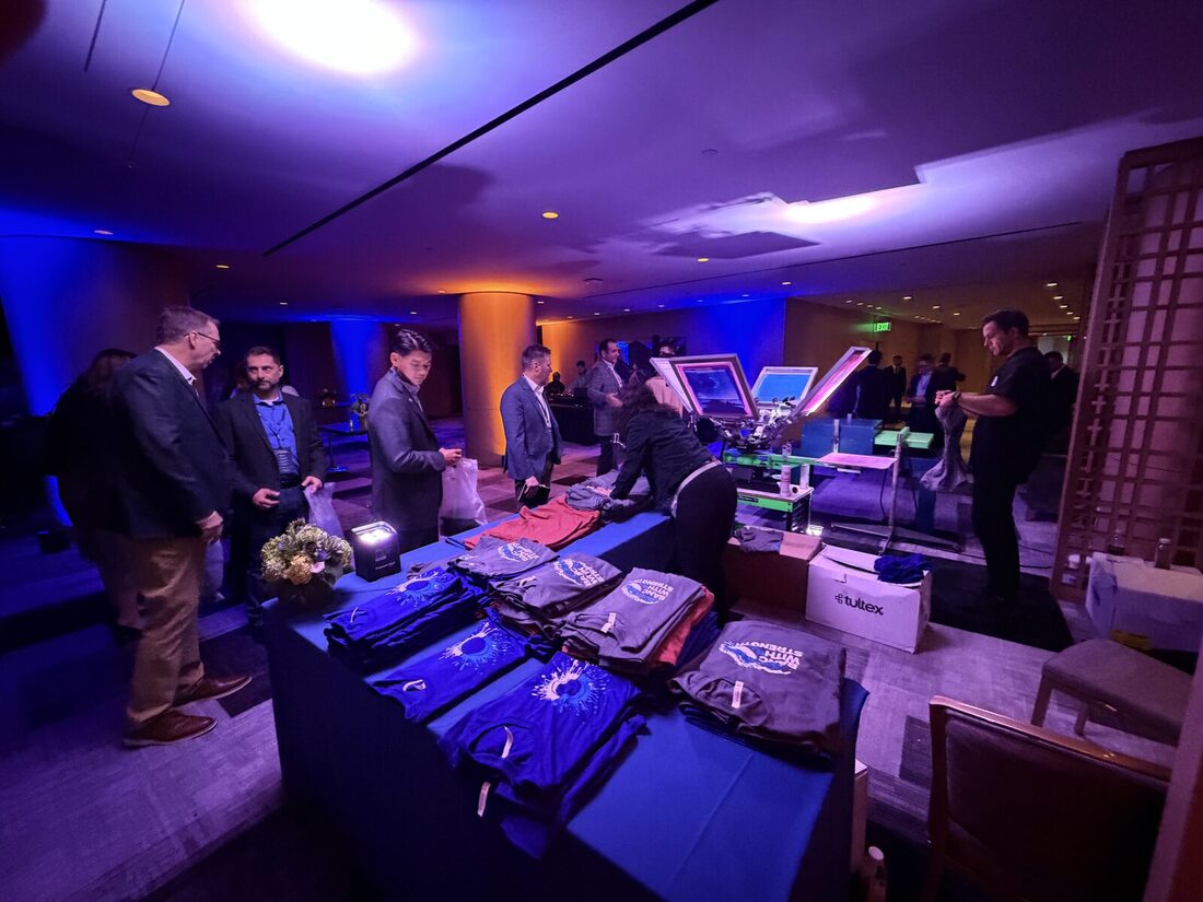 Guests browsing folded custom-printed shirts and totes at a moody, evening activation